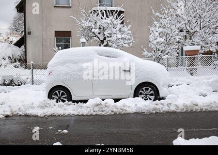 Schneebedecktes, gewöhnliches weißes Fließheck-Auto, das nach starkem Schneefall auf der Straße geparkt wurde. Weitwinkelansicht aus der Nähe, keine Personen. Stockfoto