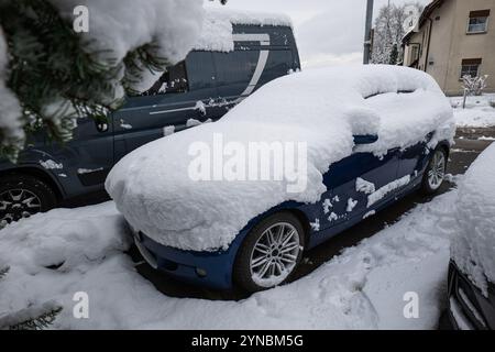 Schneebedecktes, typisches blaues Fließheck-Auto, das nach starkem Schneefall auf der Straße geparkt wurde. Weitwinkelansicht aus der Nähe, keine Personen. Stockfoto