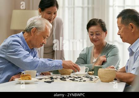 Eine Gruppe glücklicher asiatischer Senioren versammelt sich zu Hause und spielt ein chinesisches Spiel von Go Together Stockfoto