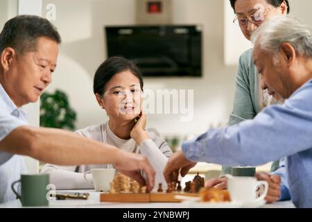 Gruppe glücklicher asiatischer Senioren, zwei Paare, die sich zu Hause treffen und gemeinsam Schach spielen Stockfoto