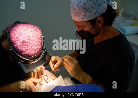 Ein Team von Chirurgen, die eine Haartransplantation mit Präzision durchführen, wobei spezielle Werkzeuge unter fokussierter Beleuchtung in einer klinischen Umgebung verwendet werden. Stockfoto
