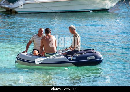 Drei Männer in einem kleinen Schlauchboot aus Gummi rudern von einer Yacht im griechischen Hafen von Agios Nikolaos in Griechenland. Stockfoto