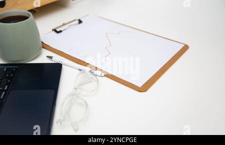 Arbeitstisch mit Diagrammen für den Büroarbeitsplatz, Bericht über Holzablage, Kaffee, Verbrauchsmaterial und Laptop. Stockfoto