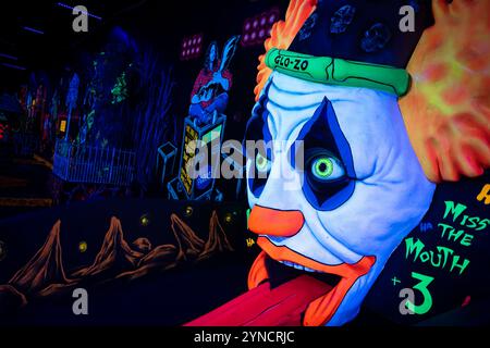 Monster Mini Golf Interior Chantilly Virginia | CHANTILLY, Virginia – Ein grinsendes „Glo-Zo“-Clown-Hindernis leuchtet bei Dunkellicht auf dem Monster Mini Golf, Teil eines Lochs, das den Spitznamen „Miss the Mouth“ trägt. Der Indoor Course verwendet UV-reaktive Farben und fluoreszierende Wandmalereien, um ein Standard-18-Loch-Minigolf-Layout in eine im Dunkeln leuchtende Attraktion zu verwandeln. Minigolfplätze wie dieser im Monsterstil sind seit den 2000er Jahren in den Vereinigten Staaten als Unterhaltungszentren für Familien ausgeweitet worden. Stockfoto