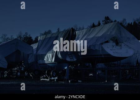 Segelboote sind abgedeckt, geschützt und außerhalb des Wassers gelagert für den Winter in der Nacht, Winterlager für das Segelboot in Finnland, Winter, kurz Stockfoto