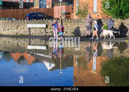 Chippenham, Wiltshire, Großbritannien, 25. November 2024. Menschen, die heruntergekommen sind, um die überfluteten Straßen im Zentrum von Chippenham zu sehen, spiegeln sich in der mit Wasser gefüllten Straße wieder. Quelle: Lynchpics/Alamy Live News Stockfoto