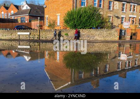 Chippenham, Wiltshire, Großbritannien, 25. November 2024. Menschen, die heruntergekommen sind, um die überfluteten Straßen im Zentrum von Chippenham zu sehen, spiegeln sich in der mit Wasser gefüllten Straße wieder. Quelle: Lynchpics/Alamy Live News Stockfoto