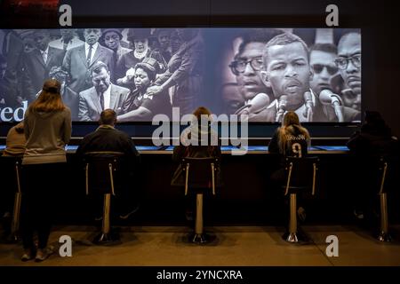 National Museum of African American History Lunch Counter Exhibit Washington DC | WASHINGTON D.C., Vereinigte Staaten – Museumsbesucher sitzen auf Chrom- und Vinyl-Hockern gegenüber einer Lunch-Theke im National Museum of African American History and Culture und sehen Archivmaterial des Bürgerrechtlers John Lewis, der sich vor einer Menschenmenge wendet. Die Ausstellung repräsentiert die Sitzplätze und Atmosphäre des separaten Woolworth-Thekens, an dem die Greensboro-Sit-ins 1960 begannen. Stockfoto