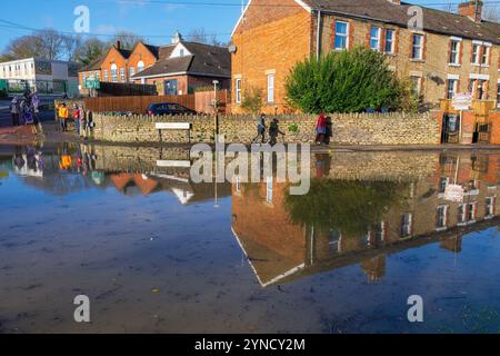 Chippenham, Wiltshire, Großbritannien, 25. November 2024. Menschen, die heruntergekommen sind, um die überfluteten Straßen im Zentrum von Chippenham zu sehen, spiegeln sich in der mit Wasser gefüllten Straße wieder. Quelle: Lynchpics/Alamy Live News Stockfoto