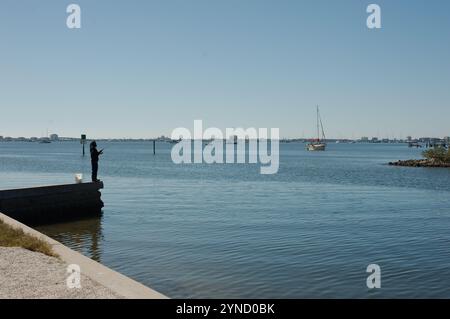 Führende Linie am Ufer des linken Mannes, der vor Gulfport, FL, angeln kann. Blick über das Outlet zur Boca Ciega Bay vom Yachthafen. Boote im Rücken ruhiges flaches Wasser. Sonnig Stockfoto