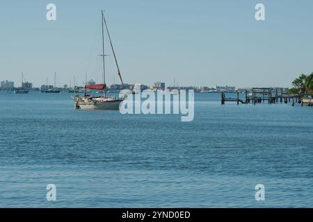 Weite Tiefsicht Gulfport, FL, USA. Blick über Outlet zum Segelboot Boca Ciega Bay mit Mast, Holzdocks, grünen Bäumen und anderen Booten. Ruhige flache Wellen. Stockfoto