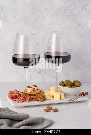 Lebensmittelfotografie von Rotwein mit Käse-Parmesan, Schinken, Oliven, Mandeln, Cracker mit Weichkäse, Weingläser, verschiedene Vorspeisen für Stockfoto