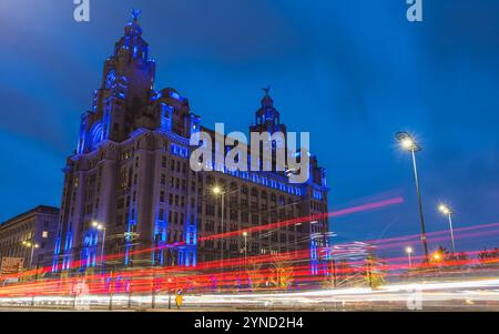 Lebhafte Verkehrswege vor dem Royal Liver Building an der Hafenpromenade von Liverpool am 24. November 2024 in der Dämmerung. Stockfoto