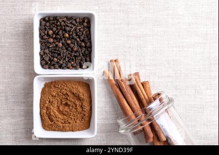 Cassia Zimtpulver und Knospen in weißen Schüsseln, klebt in einem Glasgefäß, auf Leinengewebe, mit leerem Platz für Text. Ganze und geriebene getrocknete Rinde. Stockfoto