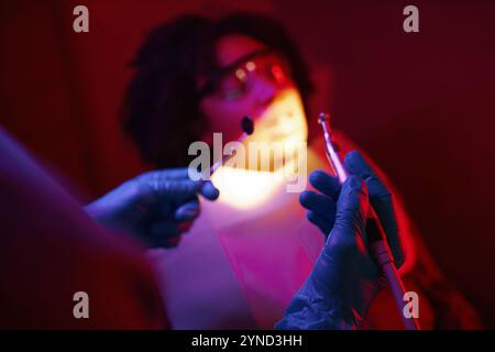 Zahnarzt, der die Zähne des Patienten unter rotem Licht reinigt Stockfoto