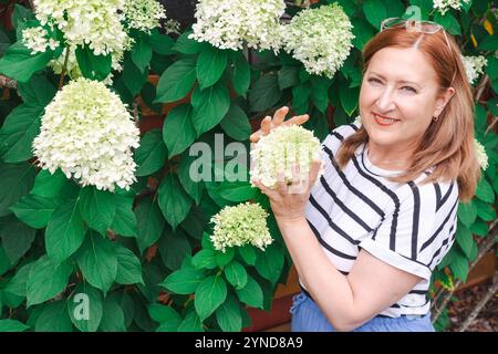 Schöne reife Frau mit einem Busch von Hortensie in voller Blüte Stockfoto
