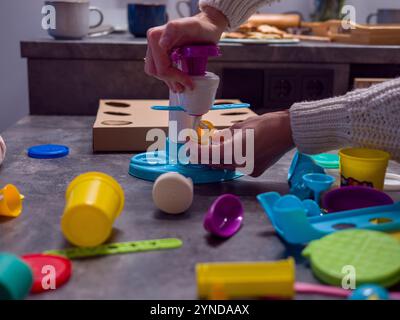 Frau genießt Spieleis-Set, macht lebendiges Spielessen auf der Küchentheke und nimmt an lustigen und lehrreichen Aktivitäten mit ihrer Familie Teil Stockfoto