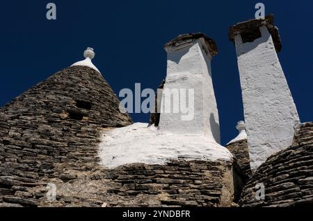 Hohe Schornsteine und Kegel auf benachbarten restaurierten Trulli in Alberobello, Apulien, Italien. Viele der traditionellen Trulli im Süden Apuliens haben konische Dächer aus Kalksteinplatten. Stockfoto