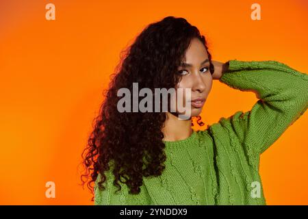 Eine auffällige Frau in grünem Pullover und Locken besticht durch ihre selbstbewusste Pose. Stockfoto