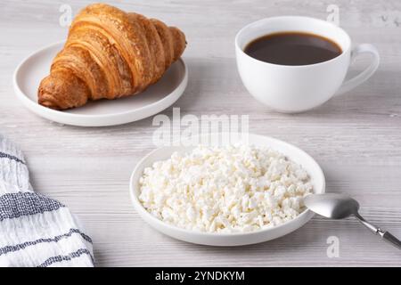 Köstliches Frühstück mit Croissant, Hüttenkäse und Kaffee auf einem Holztisch Stockfoto