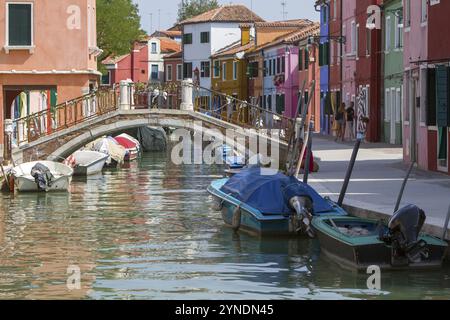 Kanal mit Brücke und farbenfrohen Häusern, umgeben von ruhig verankerten Booten in der Sonne, Burano, Venedig, Italien, Europa Stockfoto