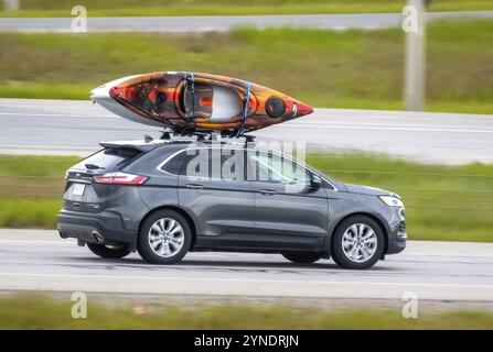 Calgary, Alberta, Kanada. Juni 2024. Ein grauer Ford Edge fährt einen Highway hinunter mit einem gesicherten orangen und weißen Kajak, der auf seinem schwarzen Dachträger montiert ist Stockfoto