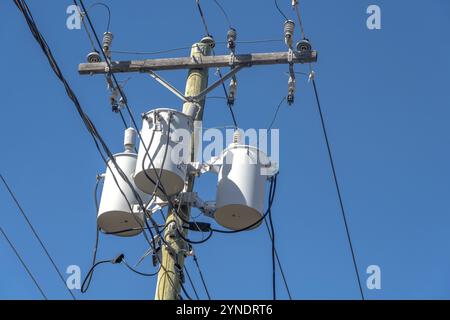 Calgary, Alberta, Kanada. April 2023. Trafobank mit drei weißen Verteilungstransformatoren an einem Pol mit blauem Himmel Stockfoto