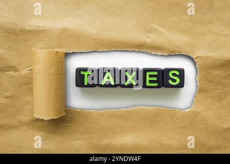 Braunes Packpapier, das zerrissen ist, um schwarze Würfel mit dem Wort Steuern zu enthüllen. Konzept Steuer Saison Stockfoto