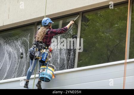 Calgary, Alberta, Kanada. Juli 2023. Eine Arbeiterin, die im Sommer ein Fenster aus einem hohen Gebäude putzt. Fenster-Waschmaschine Für Wolkenkratzer Stockfoto