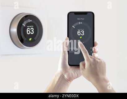 Eine Person, die eine Smartphone-Anwendung verwendet, spart Energie mit einem drahtlosen intelligenten Thermostat auf weißem Hintergrund Stockfoto