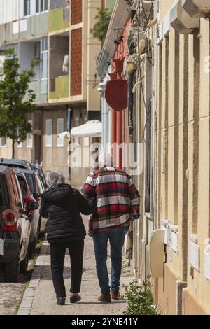 Zwei ältere Menschen, die den Rücken abgewandt haben, gehen die Straße hinunter, wo ihre Gesichter nicht zu sehen sind, wie sie Hände in einer Szene der Liebe und des Aff halten Stockfoto