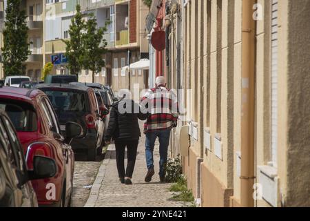 Zwei ältere Menschen, die den Rücken abgewandt haben, gehen die Straße hinunter, wo ihre Gesichter nicht zu sehen sind, wie sie Hände in einer Szene der Liebe und des Aff halten Stockfoto