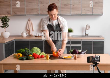 Junger Mann mit frischem Gemüse, der Kochvideo in der Küche aufnimmt Stockfoto