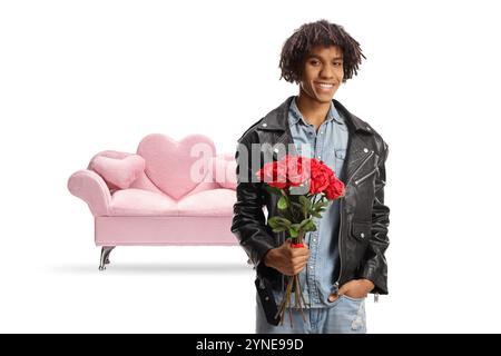 Junger Mann aus afroamerikaner vor einem rosa Sofa, der einen Strang Rosen auf weißem Hintergrund hält Stockfoto