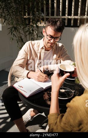 Junger Mann, der sich Notizen macht während eines Kaffeetreffens im Freien Stockfoto