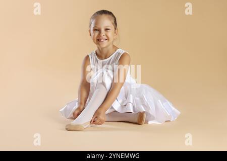 Kleine Ballerina, die spitzenschuhe vor beigefarbenem Hintergrund anzieht Stockfoto