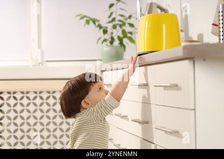 Kleiner Junge, der mit Toaster in der Küche spielt. Gefährliche Situation Stockfoto