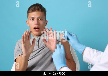 Nadelphobie. Der verängstigte Mann macht Stop Geste in der Nähe des Arztes mit Spritze und Fläschchen auf hellblauem Hintergrund Stockfoto