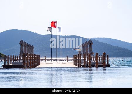 Hölzerner Pier am Meer und Reflexion auf dem Wasser türkische Flagge und Hotelbanner am Horizont Stockfoto