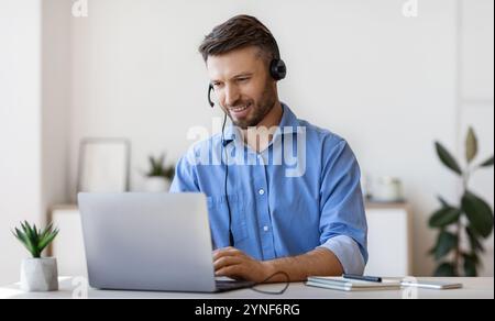 Schöner Junger Mann In Headset Studie Online, Beobachten Webinar Auf Laptop Stockfoto