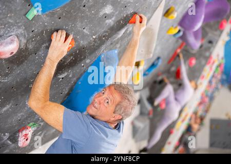 Der ältere Mann klettert ohne Seile und Gurte an der Boulderwand Stockfoto