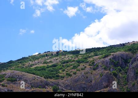 Einmotoriges Propellerflugzeug, das in geringer Höhe in Bodennähe manövriert. Blauer Himmel und Hügel im Hintergrund. Stockfoto