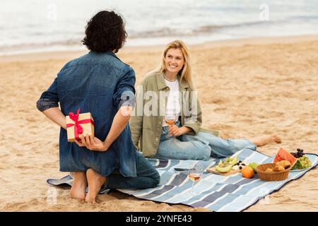 Ein Paar genießt ein Picknick am Strand, während es einen besonderen Anlass bei Sonnenuntergang feiert Stockfoto