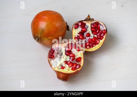 Ein ganzer Granatapfel und anderthalb auf einer hellen Holzoberfläche. Stockfoto