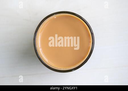 Heißer Milchtee oder dudh Cha in einer Glasschale, auf einer hellen Holzoberfläche gehalten. Draufsicht. Stockfoto