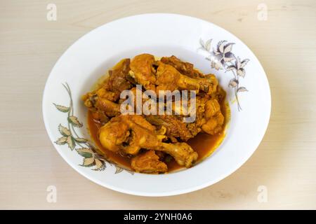 Hausgemachtes, köstliches Hühnchen-Bhuna-Curry, serviert auf einem weißen Teller auf einer hellen Holzoberfläche. Ein schmackhaftes bengalisches Gericht (Bangladesch). Stockfoto