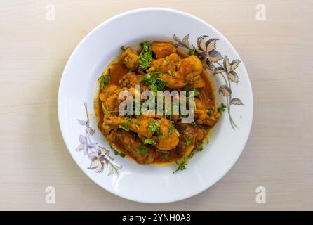 Hausgemachtes, köstliches Hühnchen-Bhuna-Curry, garniert mit Korianderblättern, serviert auf einem weißen Teller. Blick von oben auf ein schmackhaftes bengalisches Gericht. Stockfoto