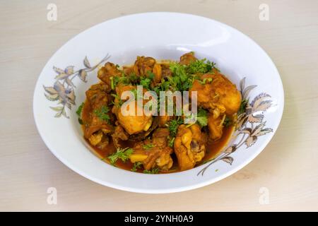 Hausgemachtes, köstliches Hühnchen-Bhuna-Curry, garniert mit Korianderblättern, serviert auf einem weißen Teller. Ein schmackhaftes bengalisches Gericht. Stockfoto