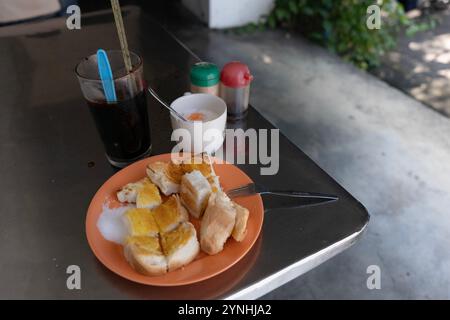 Ein typisches 'malaysisches Frühstück' mit Toastbrot mit Butter und Zucker, einem halbgekochten Ei und einem Glas Eiskaffee, serviert an einem Straßenstand. Stockfoto