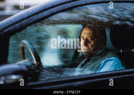 Ein Senior sitzt in einem geparkten Auto und blickt nachdenklich aus dem Fenster. Die ruhige Umgebung draußen steht im Kontrast zu seinem kontemplativen Ausdruck d Stockfoto